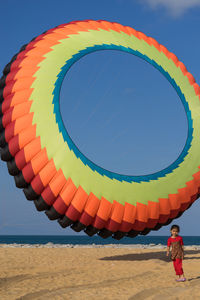 Full length of girl standing by colorful large ring kite at beach