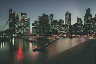 Illuminated buildings by river against sky in city at night