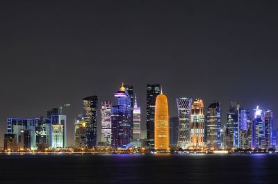 Illuminated buildings by sea against sky at night