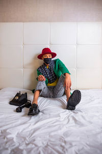 Full length of man sitting on bed against wall