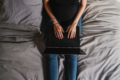 Midsection of woman using laptop on bed