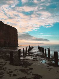 Wooden posts on beach against sky during sunset