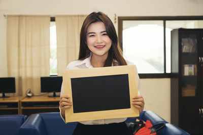 Portrait of smiling businesswoman holding blank slate while standing in office