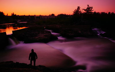 Rear view of silhouette man looking at lake during sunset