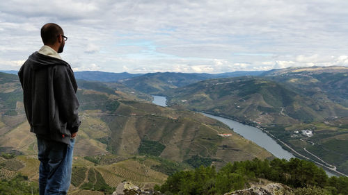 Rear view of man standing on cliff against mountains