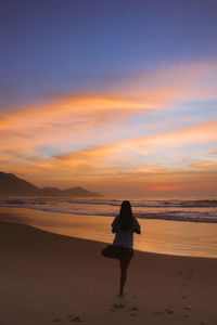 Rear view of man standing on beach during sunset