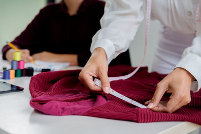 Midsection of fashion designer with colleague measuring cloth