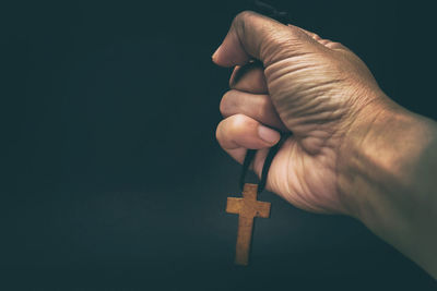 Close-up of hand holding cross against black background