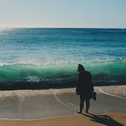 Rear view of man standing at beach against clear sky