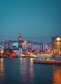 Buildings by river against clear blue sky