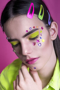 Close up studio portrait of a young girl in neon jacket on pink background with inspired make up