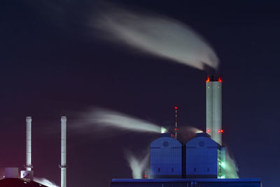 Smoke emitting chimneys against sky at night