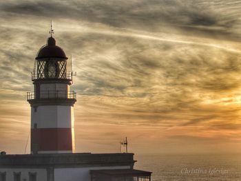 Lighthouse by sea against sky during sunset