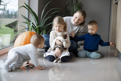Mother with her three children playing with a cat on the floor at home