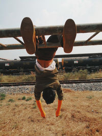 Rear view of man hanging upside down climbing frame against sky