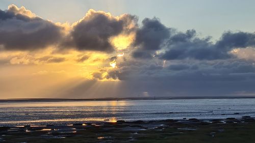 Sunlight streaming on sea against sky during sunset