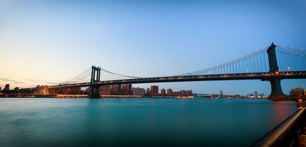 Low angle view of manhattan bridge over river against clear sky during sunset