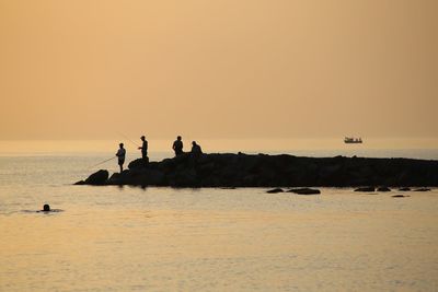 Silhouette people on sea against clear sky during sunset