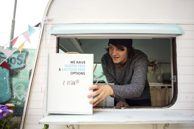 Male owner looking away while placing sign at window on food truck