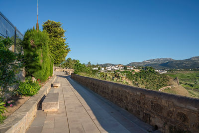 Footpath amidst buildings against clear blue sky