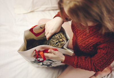 Woman with cat in bag on bed