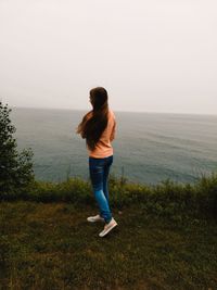 Full length of woman standing on cliff by sea against sky