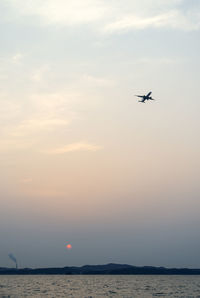 Airplane flying over sea against sky during sunset