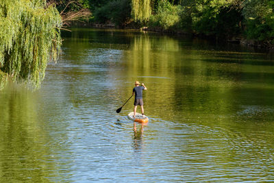 Rear view of man paddling on sup board on river.