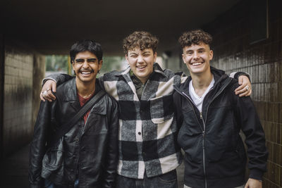 Happy teenage boy with arms around male friends standing at underpass