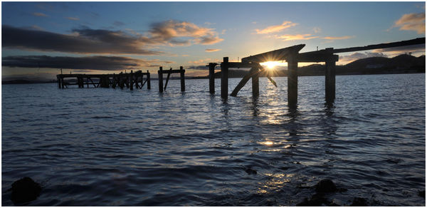 Silhouette wooden posts in sea against sky during sunset