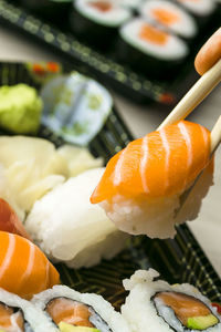 Cropped hand having sushi and sashimi in box on table