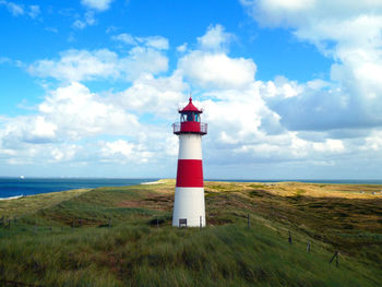 A delightful list-ost lighthouse right in a center of picturesque landscape and summer cloudy sky