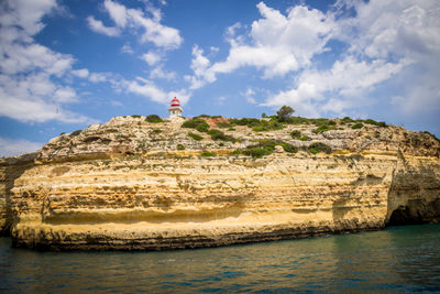 Lighthouse on rock by sea against sky