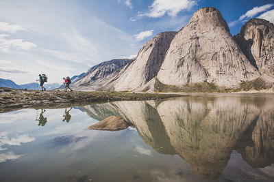 Reflection of two backpackers hiking below steep mountains