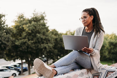 Thoughtful mature woman sitting with laptop on terrace at sunset