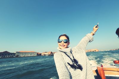 Portrait of woman wearing sunglasses on boat in sea against clear blue sky