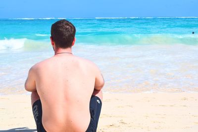 Rear view of shirtless man looking at seascape