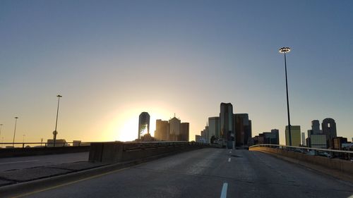 Empty road leading towards buildings in city against sky during sunset