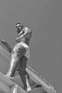 Low angle view of shirtless muscular man standing against clear sky