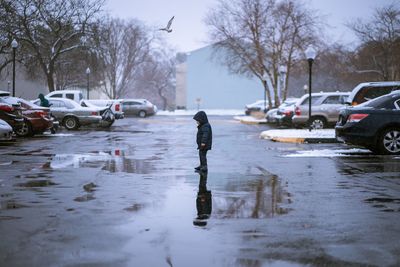 Side view of boy standing on wet footpath during winter