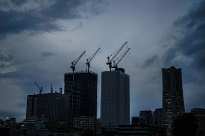 Cranes by buildings against sky in city