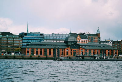 Buildings by river against sky in city