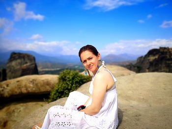 Portrait of smiling young woman sitting against sky