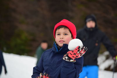 Smiling boy holding snowball while standing outdoors