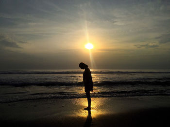 Silhouette of people standing on beach at sunset