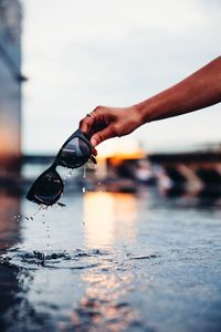 Close-up of hand holding wet glass against sky