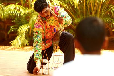 Rear view of man looking at artist performing in traditional clothing against plants