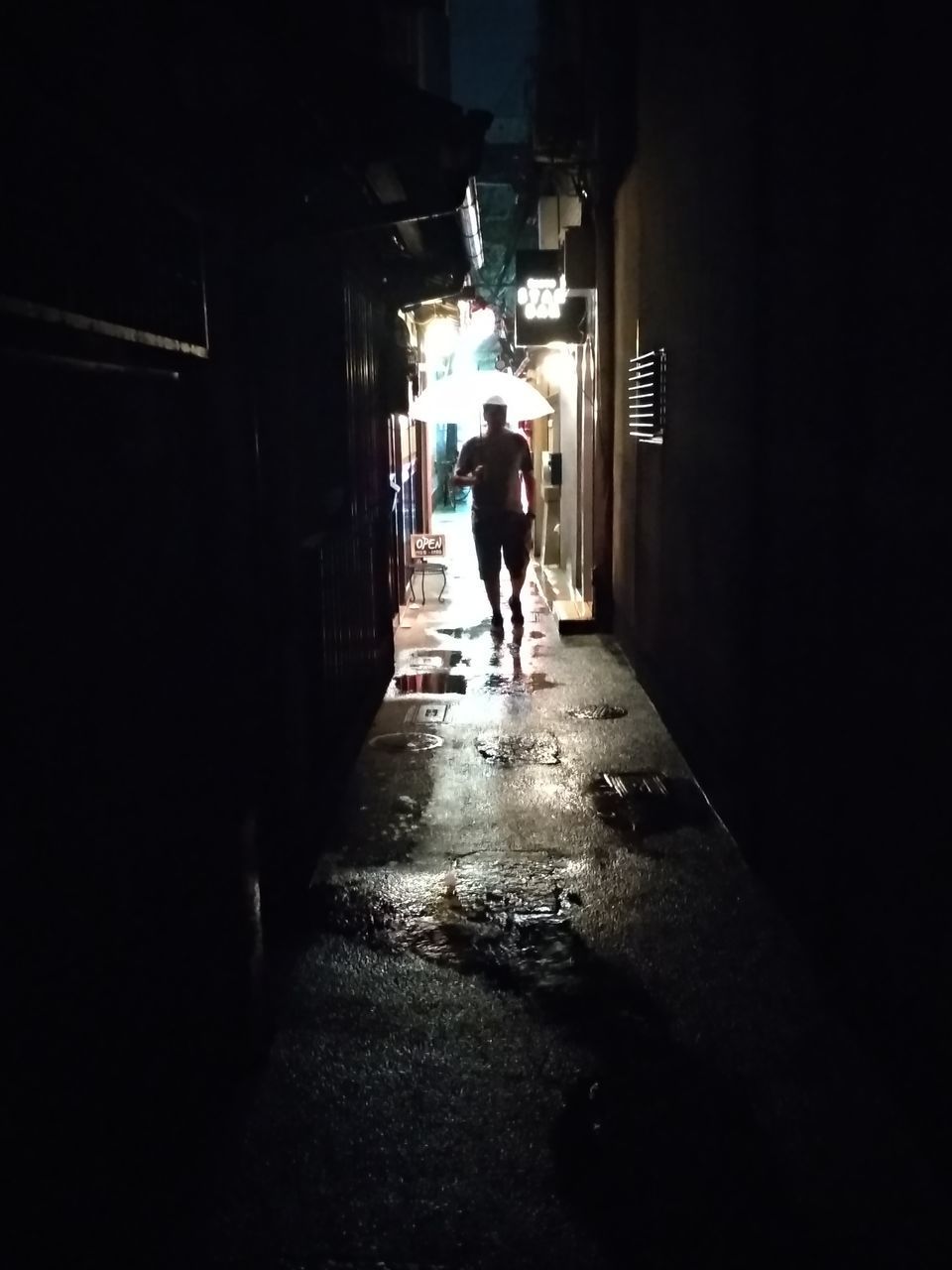 MAN WALKING ON NARROW ALLEY AMIDST BUILDINGS IN CITY