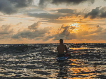 Man in sea against sky during sunset