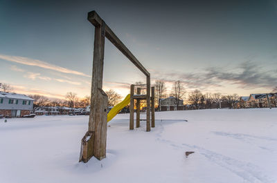 Snow covered field by building against sky during sunset